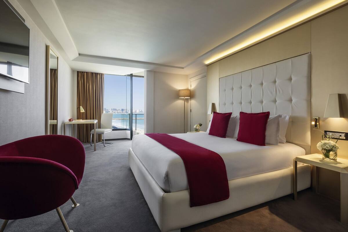 A hotel room with a large bed, a desk, a chair, and a view of the city.