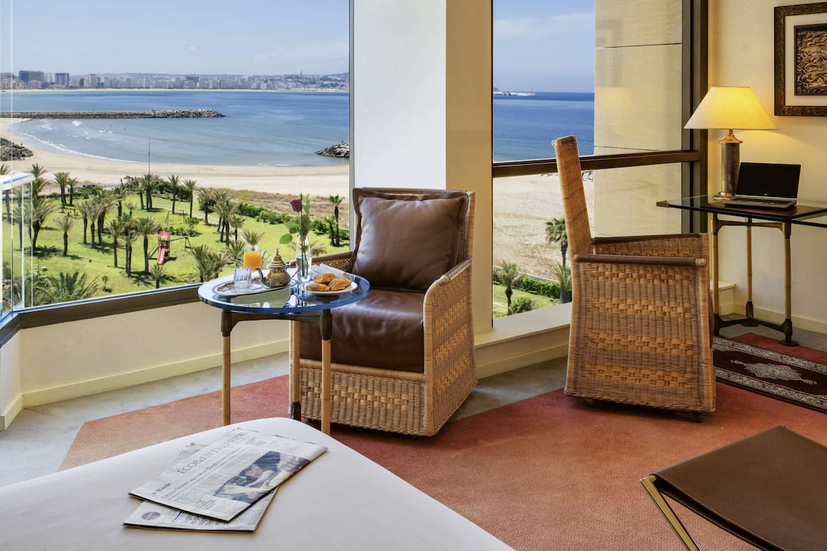 A room with a view of the beach, a laptop on a table, and a newspaper on the floor.