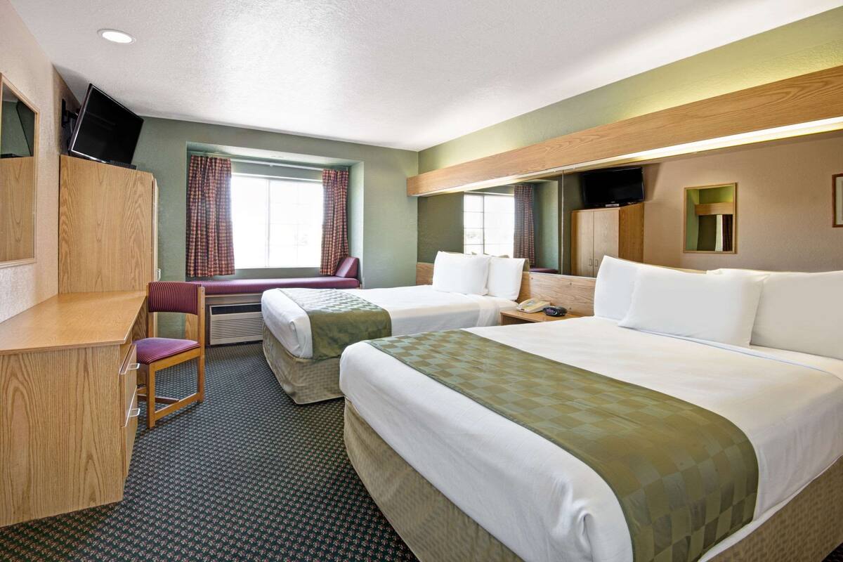 A hotel room with two beds, a desk, a chair, a television, and a window with curtains.