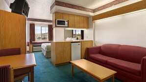 Une pièce de taille modeste, avec une table en bois, un canapé rouge, une kitchenette équipée d’un four à micro-ondes et d’un petit réfrigérateur.