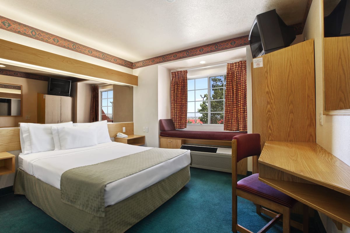 A hotel room with a large bed, a desk, a chair, a TV, and a window with curtains.