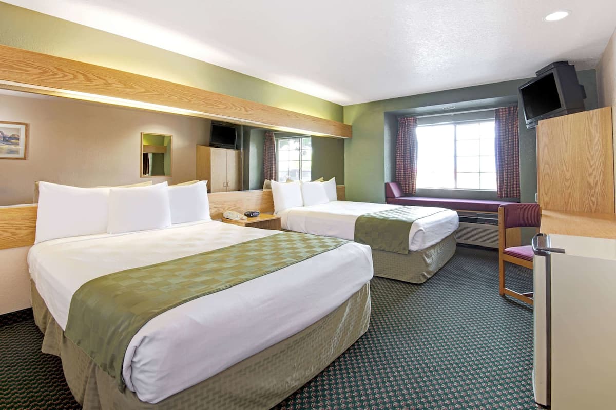 A hotel room with two beds, a television, a desk, and a chair.