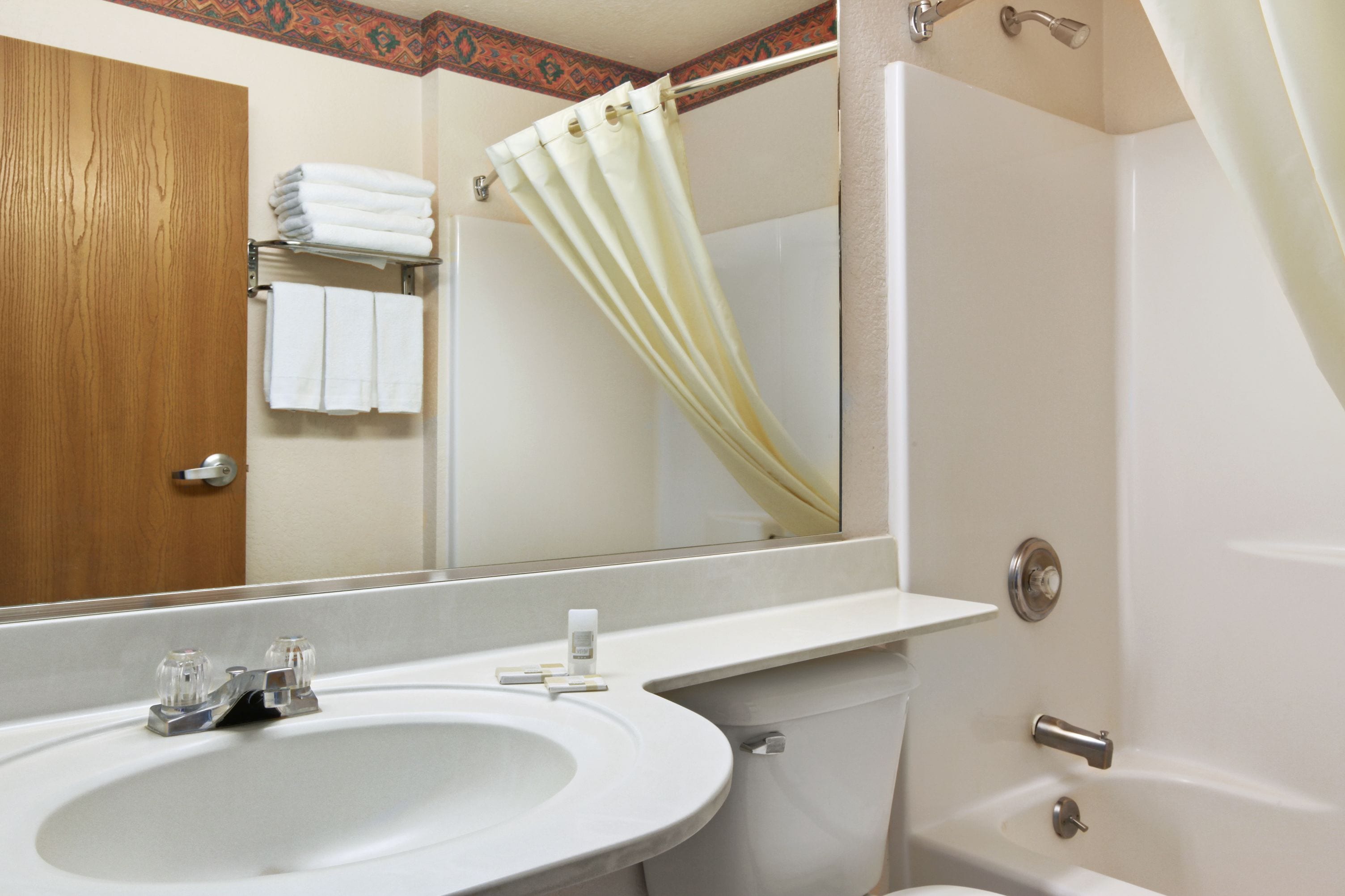 A bathroom with a sink, mirror, shower curtain, and a towel rack with folded towels.