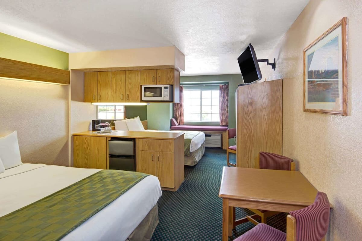 A hotel room with a bed, a desk, a chair, a microwave, a television, and a window with curtains.