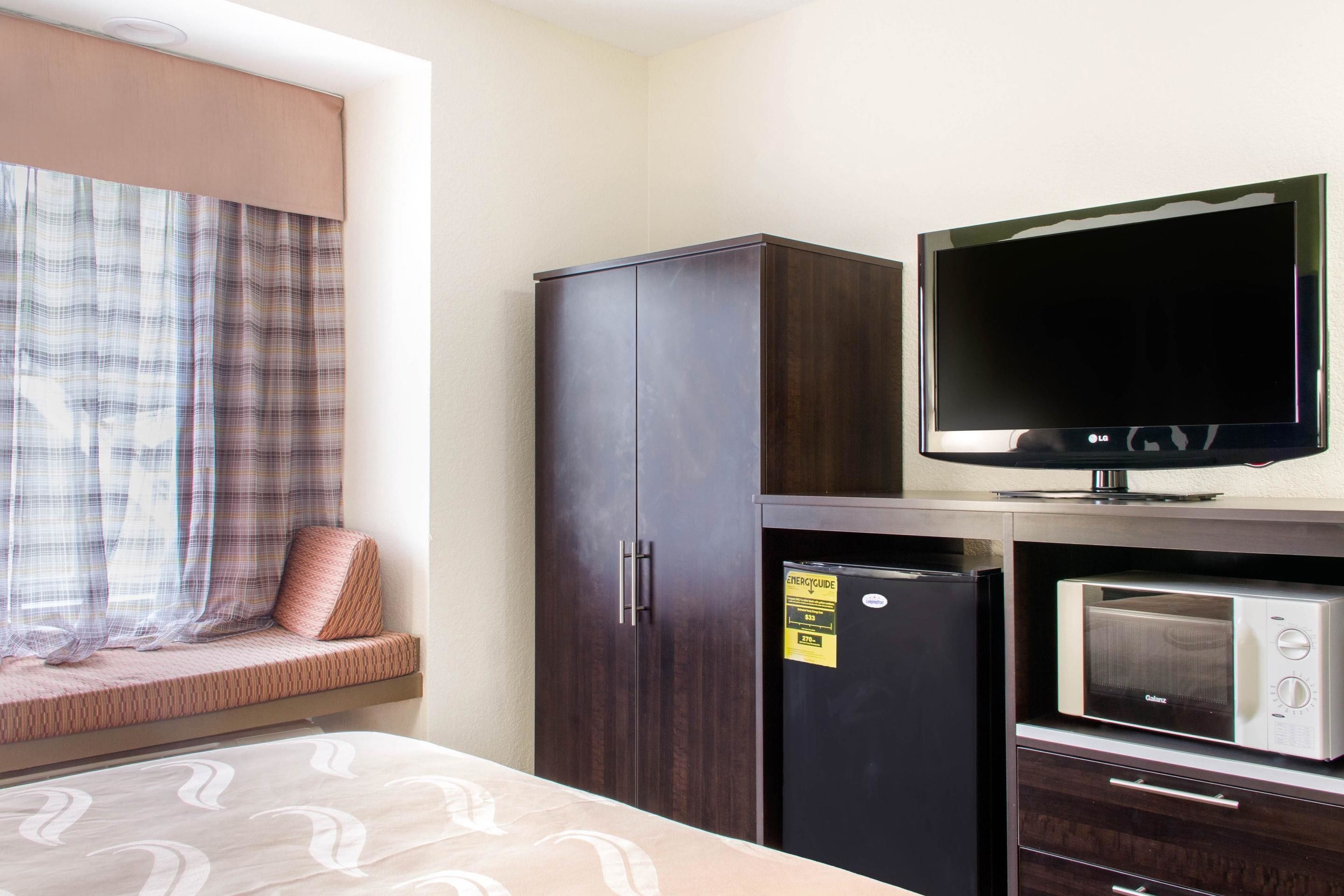 A hotel room with a bed, a television, a microwave, and a wardrobe.