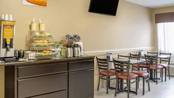 Una barra de desayuno con opciones de gofres y café, un televisor de pantalla plana y una zona de estar con sillas y mesas.