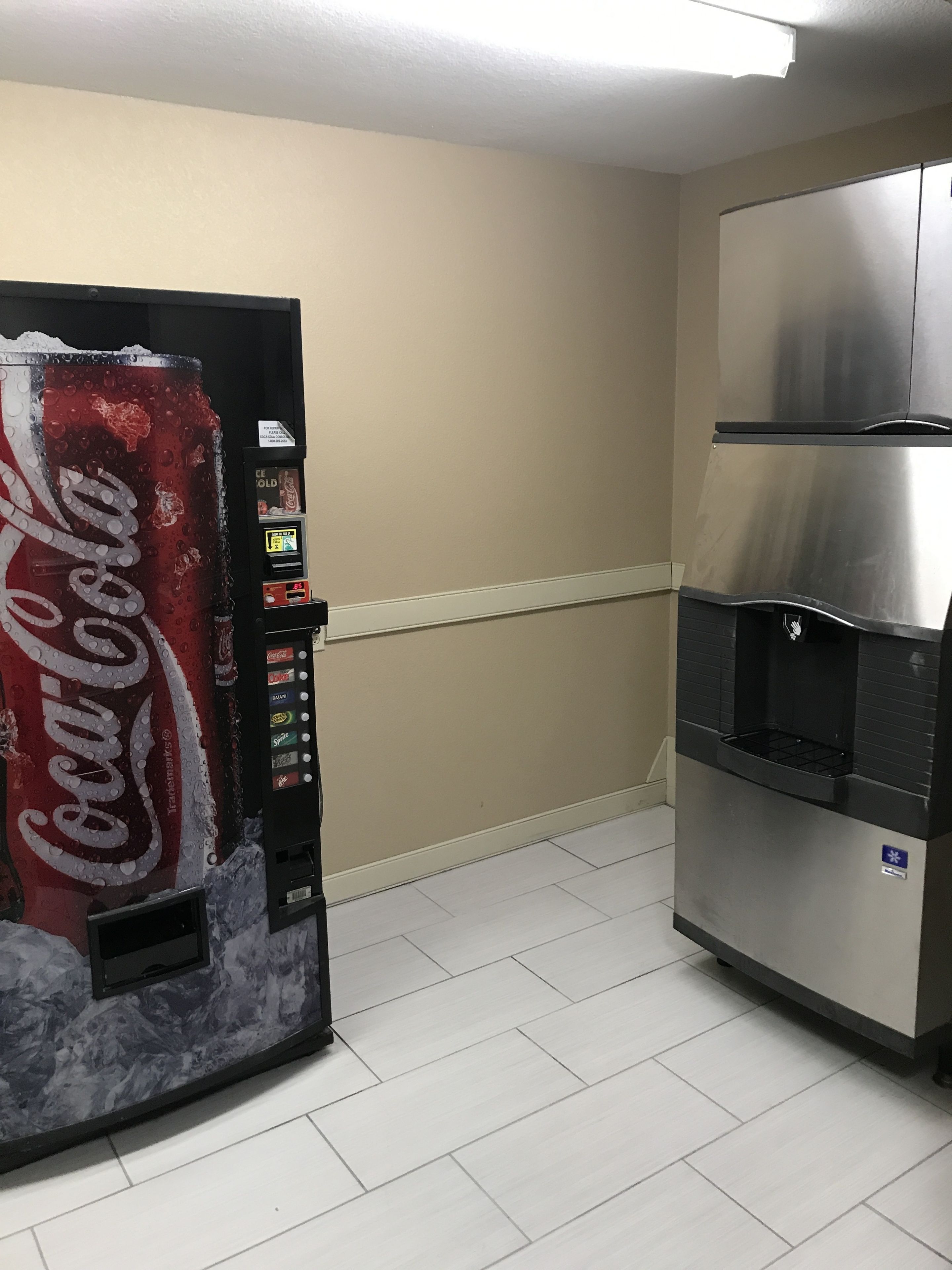 A vending machine with a Coca-Cola logo, a stainless steel refrigerator, and a tiled floor.