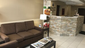 A reception area with a brown sofa, a small table with magazines, a stone-textured counter, and a wall with a sign promoting breakfast.