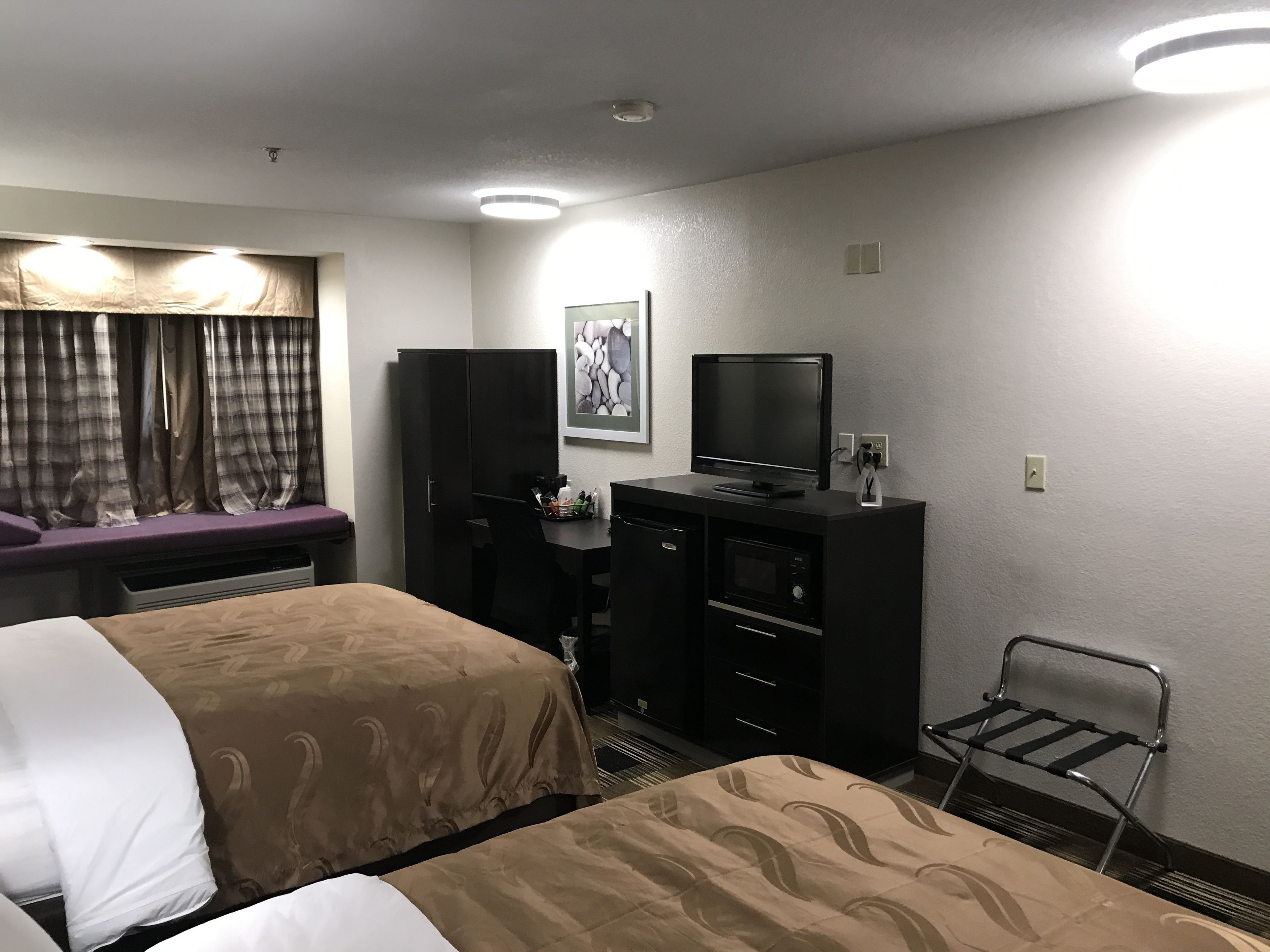 A hotel room with two beds, a desk with a television, a chair, and a window with curtains.