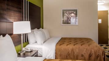 Habitación de hotel con una cama, una mesita de noche con lámpara, un teléfono y un cuadro en la pared.