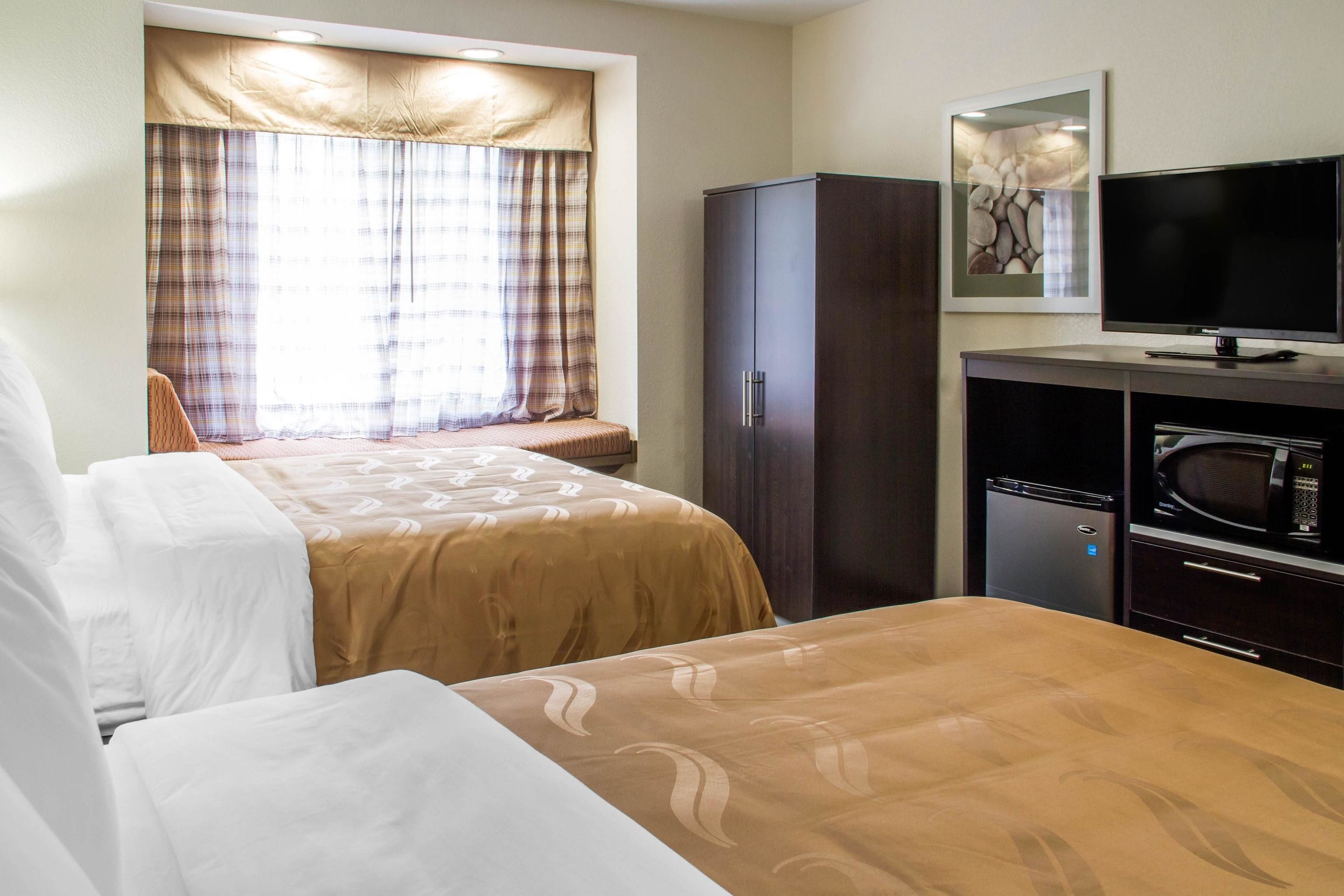 A hotel room with two beds, a television, a microwave, and a cabinet.