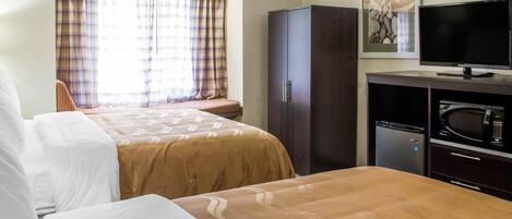 A hotel room with two beds, a television, a microwave, and a cabinet.