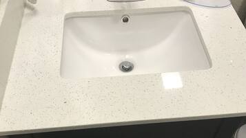 A bathroom sink with a white speckled countertop, a chrome faucet, and a soap dispenser.