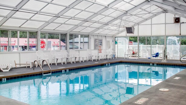 An indoor swimming pool with clear water, white chairs, and a covered area with large windows.