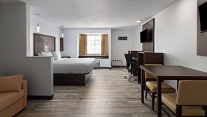 Ein Hotelzimmer mit einem Bett, einem Schreibtisch, einem Stuhl, einem Fernseher und einem Fenster mit Vorhängen.