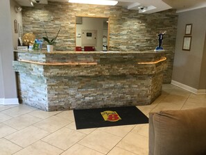 Un espace d’accueil avec un mur en pierre, un comptoir de réception, un détecteur d’incendie et un tapis orné du logo Super 8.