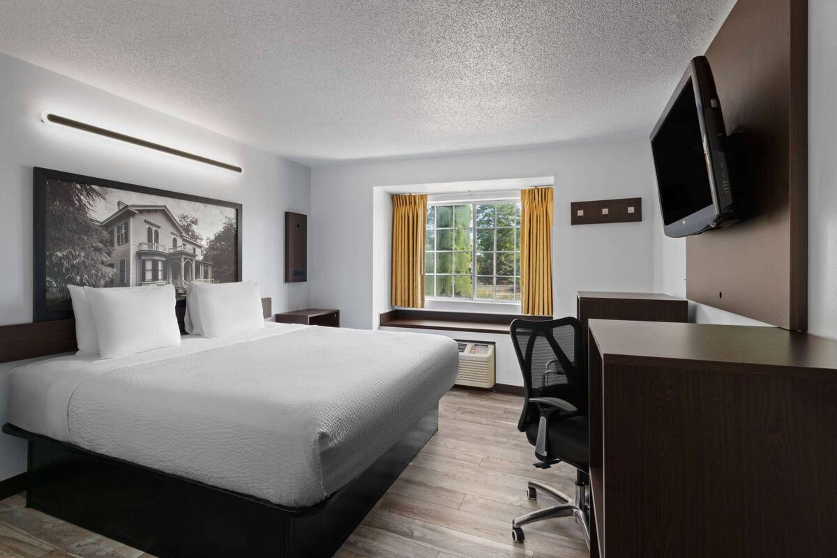 Habitación de hotel con una cama grande, un escritorio, una silla, un televisor y una ventana con cortinas.