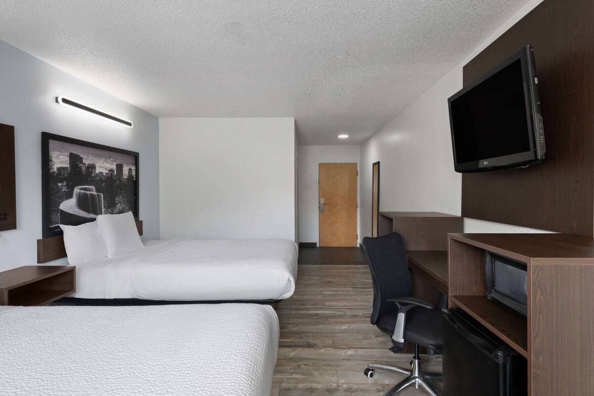 Habitación de hotel con dos camas, un escritorio, una silla, un televisor y una puerta al fondo.