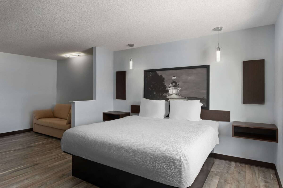 Una habitación de hotel moderna con una cama grande, un sillón color arena y una estantería de pared.