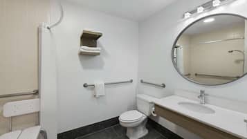 A bathroom with a toilet, sink, mirror, towel rack, and grab bars.