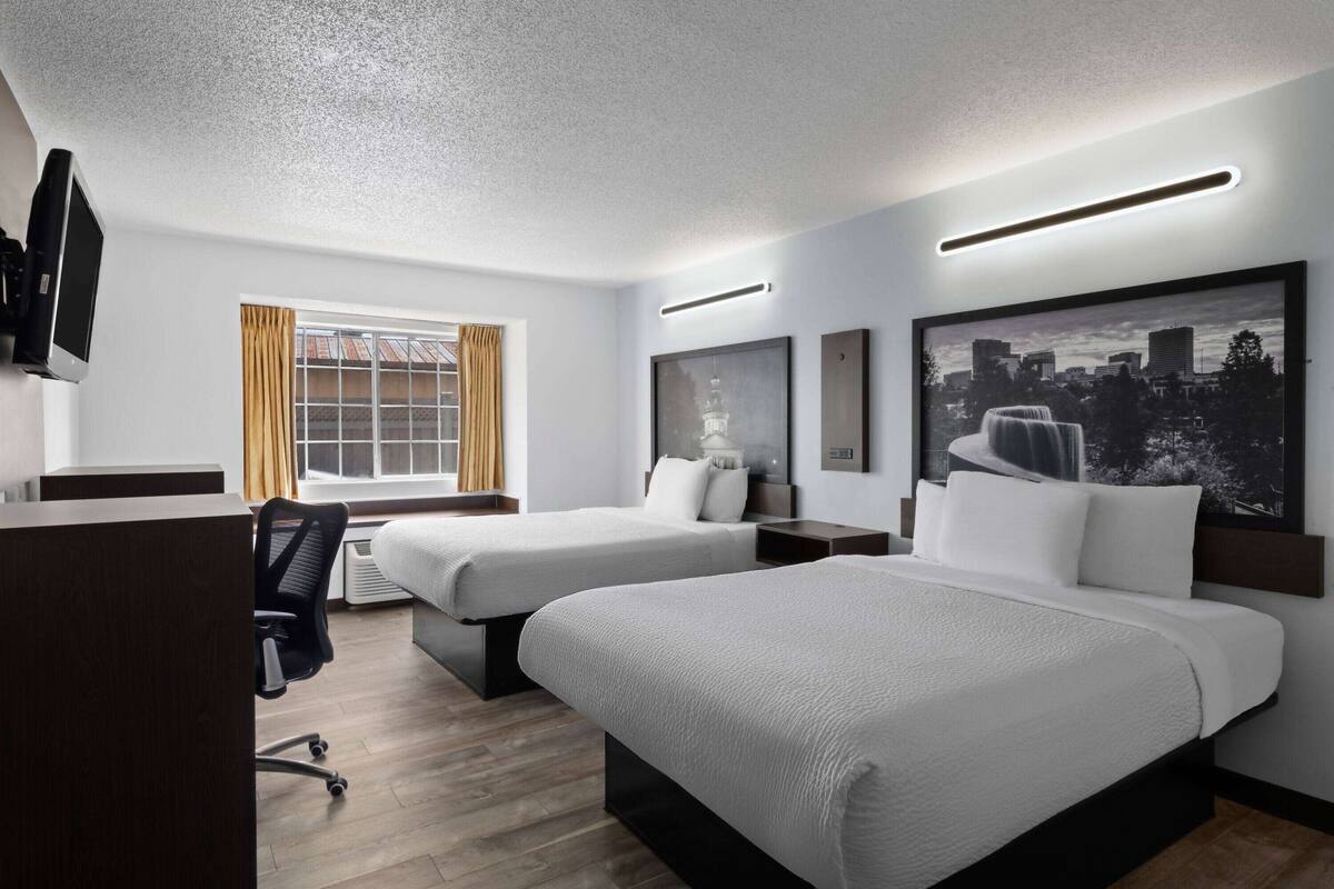 Habitación de hotel con dos camas, un escritorio, una silla, un televisor y una ventana con cortinas.