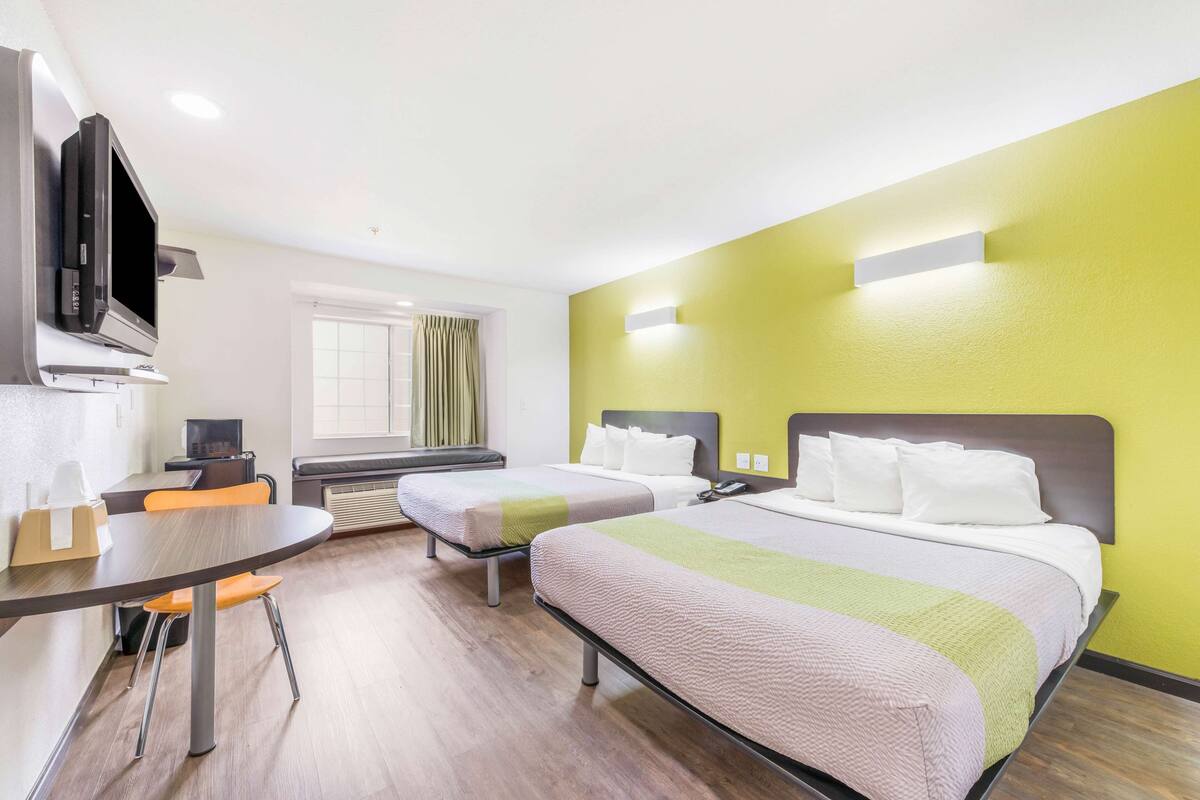 Hotellihuone, jossa on kaksi sänkyä, työpöytä, televisio ja ikkuna, jossa on verhot.