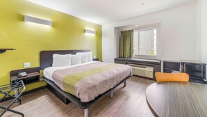 Una camera d'albergo con un letto, un comodino, una sedia e un tavolino con una sua poltrona.