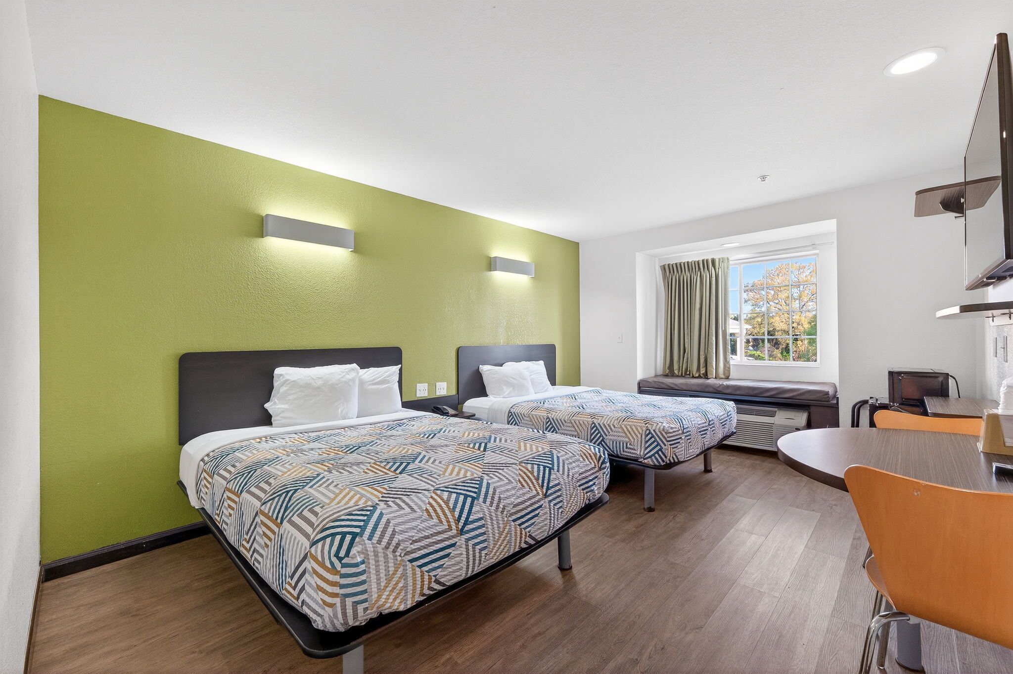 Habitación de hotel con dos camas, una mesa de comedor y un televisor.