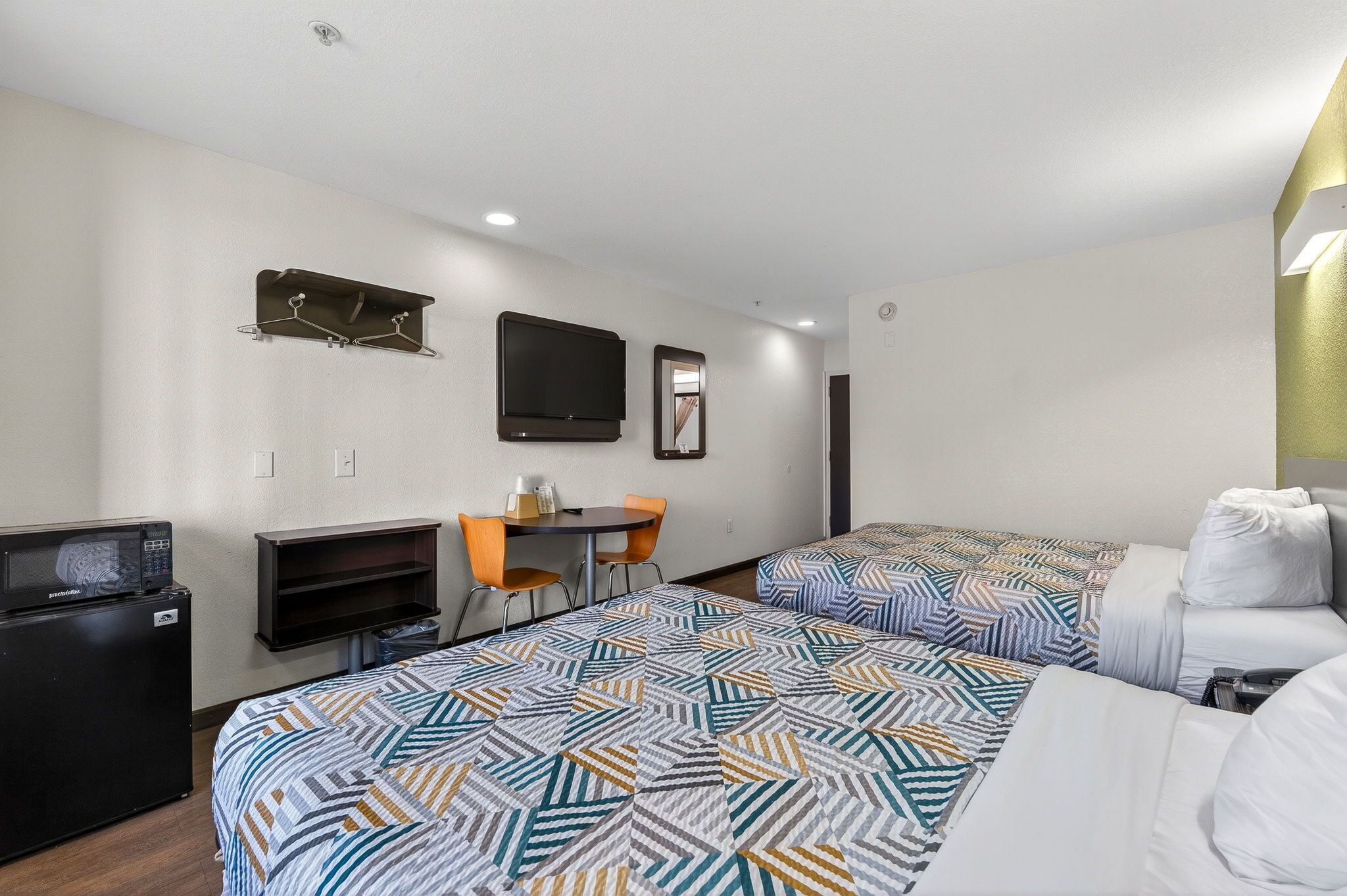 A hotel room with two beds, a desk, a chair, a TV, and a microwave.