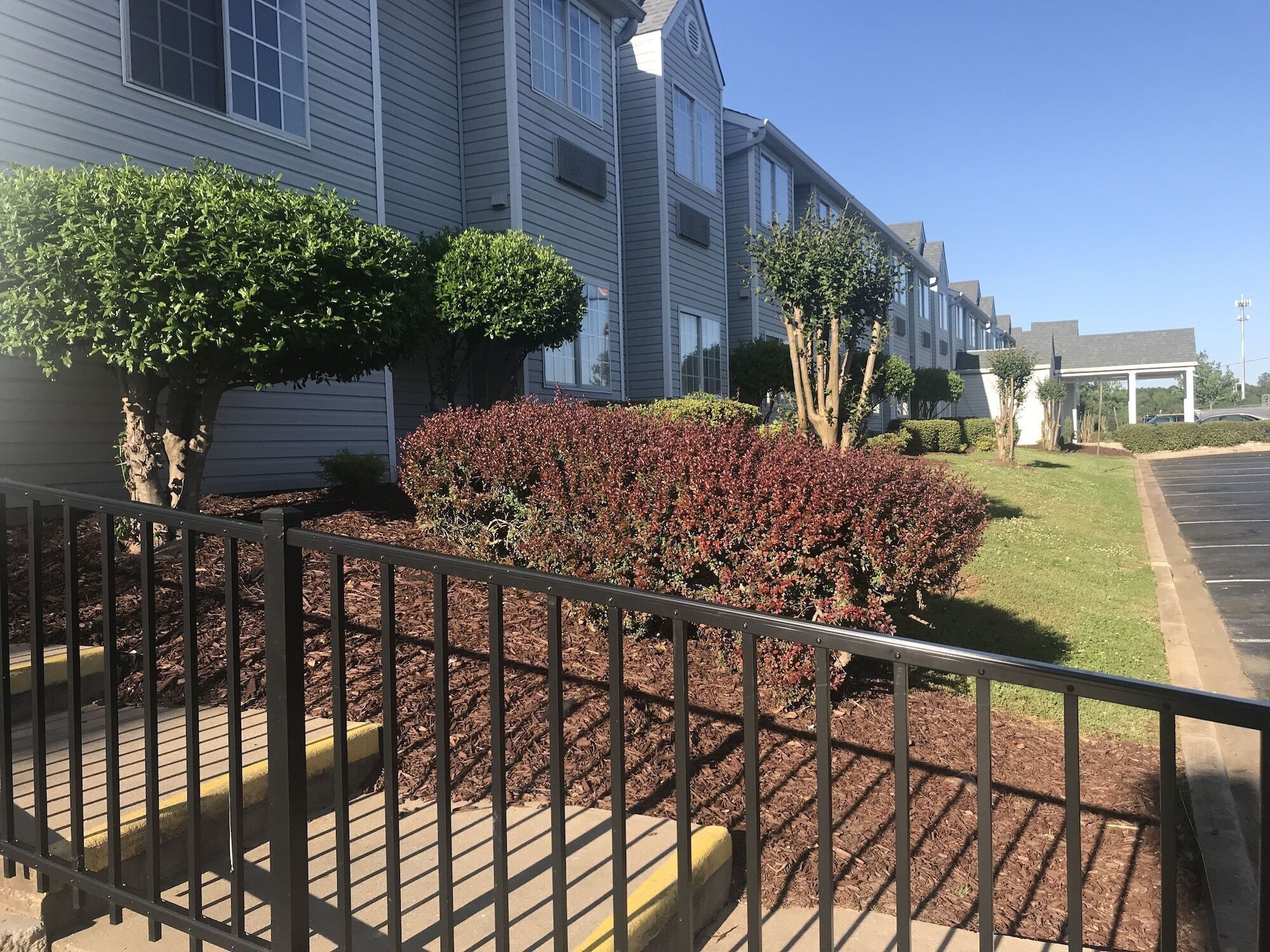 A residential building with a well-maintained garden, a parking area, and a clear sky.