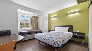Habitación de hotel con cama, escritorio, silla, ventana con cortinas y vista a árboles.