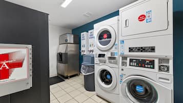 A laundry facility with stacked washers and dryers, a trash bin, and a refrigerator.