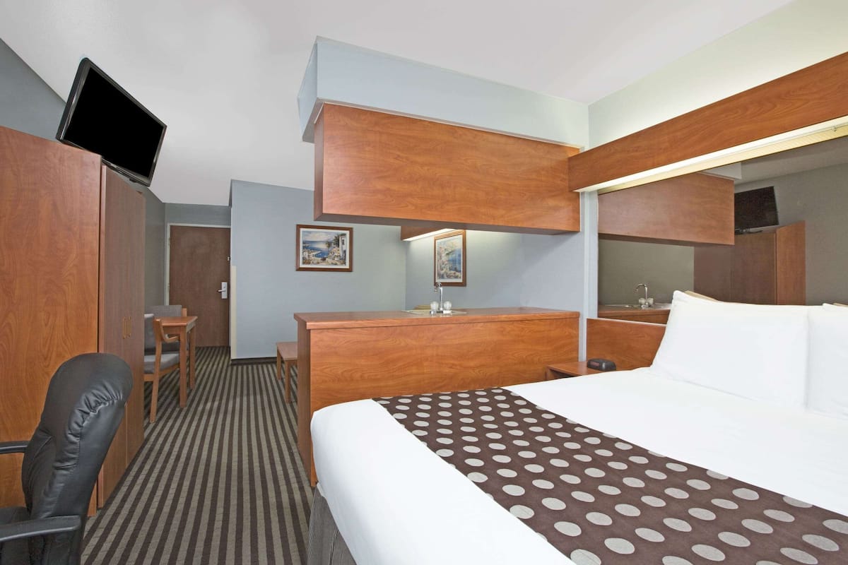 Habitación de hotel con cama, escritorio, silla, televisor y baño.