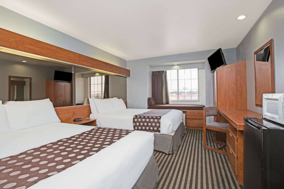 Ein Hotelzimmer mit zwei Betten, einem Schreibtisch, einem Sessel, einem Fernseher und einem Kühlschrank.