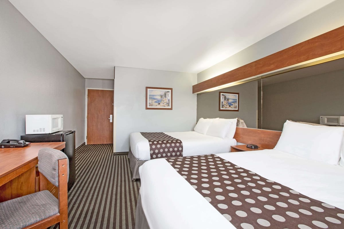Ein Hotelzimmer mit zwei Betten, einem Schreibtisch, einem Stuhl, einer Mikrowelle und einer Tür.