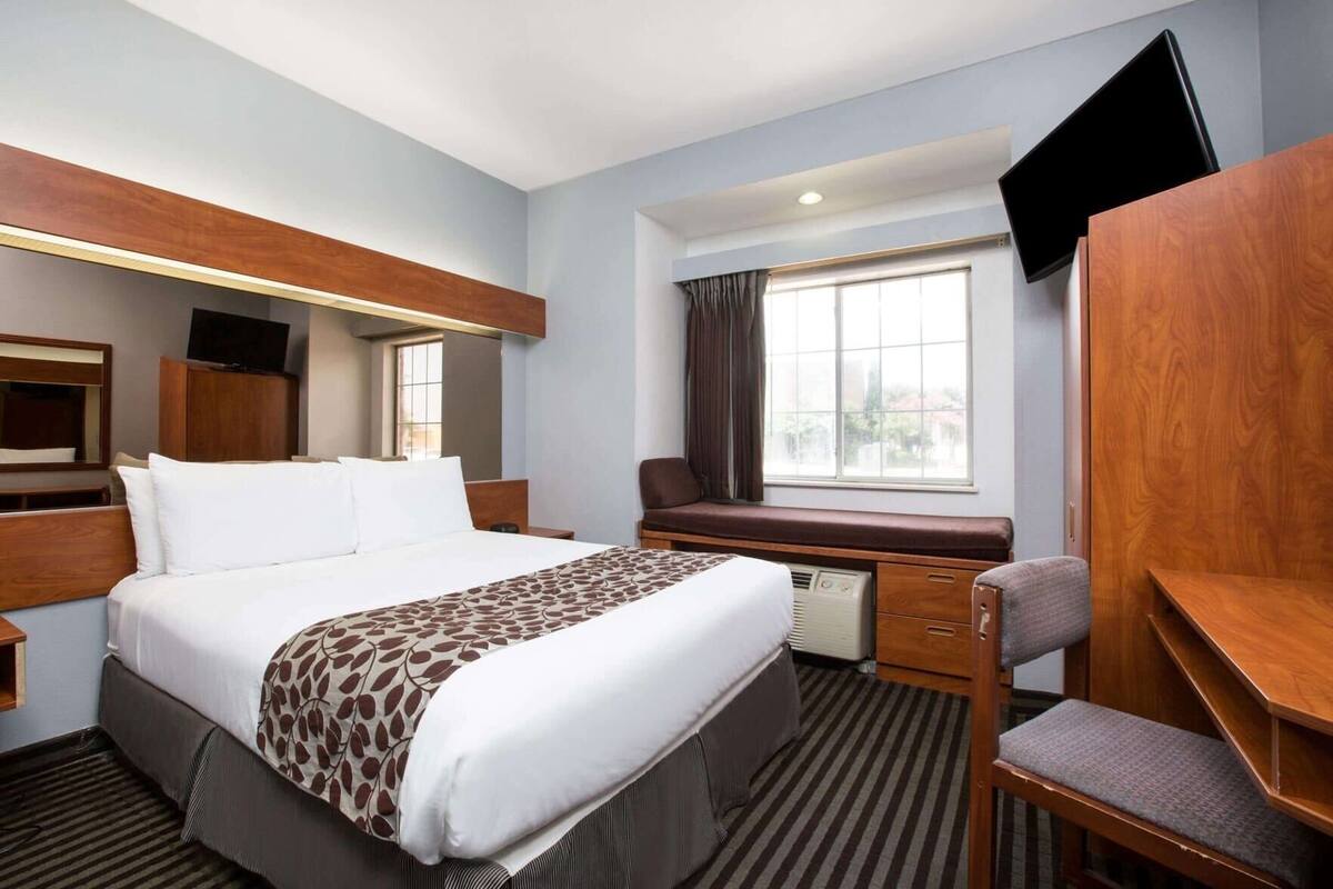Habitación de hotel con cama, escritorio, silla, televisor y ventana.