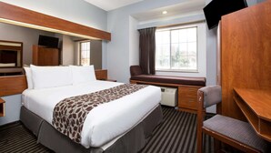 Una habitación de hotel con una cama grande, un escritorio, una silla, un televisor y una ventana con cortinas.