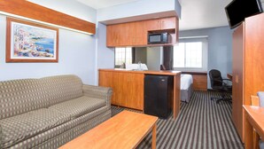 Una habitación de hotel compacta con kitchenette, un sofá, una mesita, un televisor y una ventana.