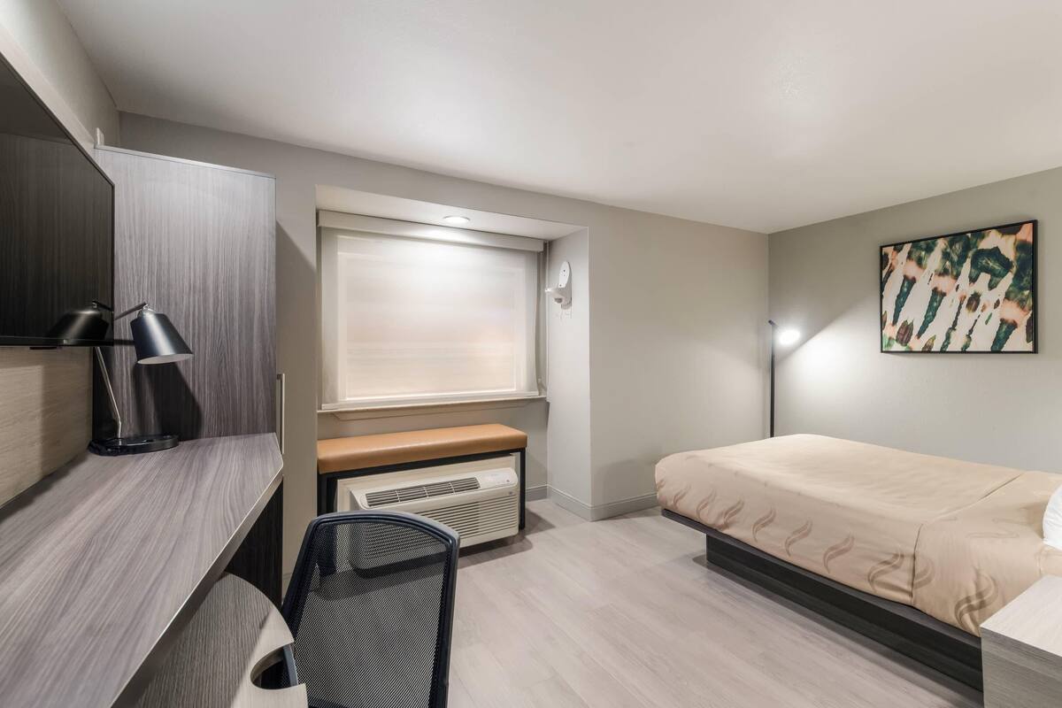 Une chambre moderne équipée d’un bureau, d’une chaise, d’un lit et d’une fenêtre avec des stores.
