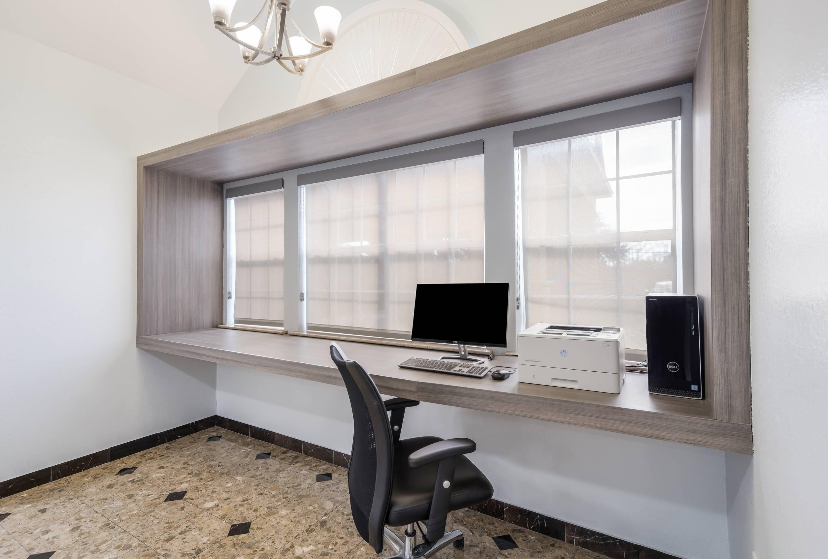 A workspace with a computer, printer, and chair, near a window with blinds.