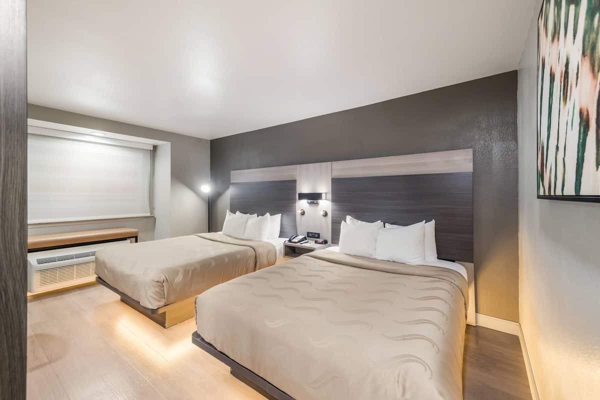 Une chambre d’hôtel moderne avec deux lits, un banc, une table de chevet et un grand tableau abstrait accroché au mur.