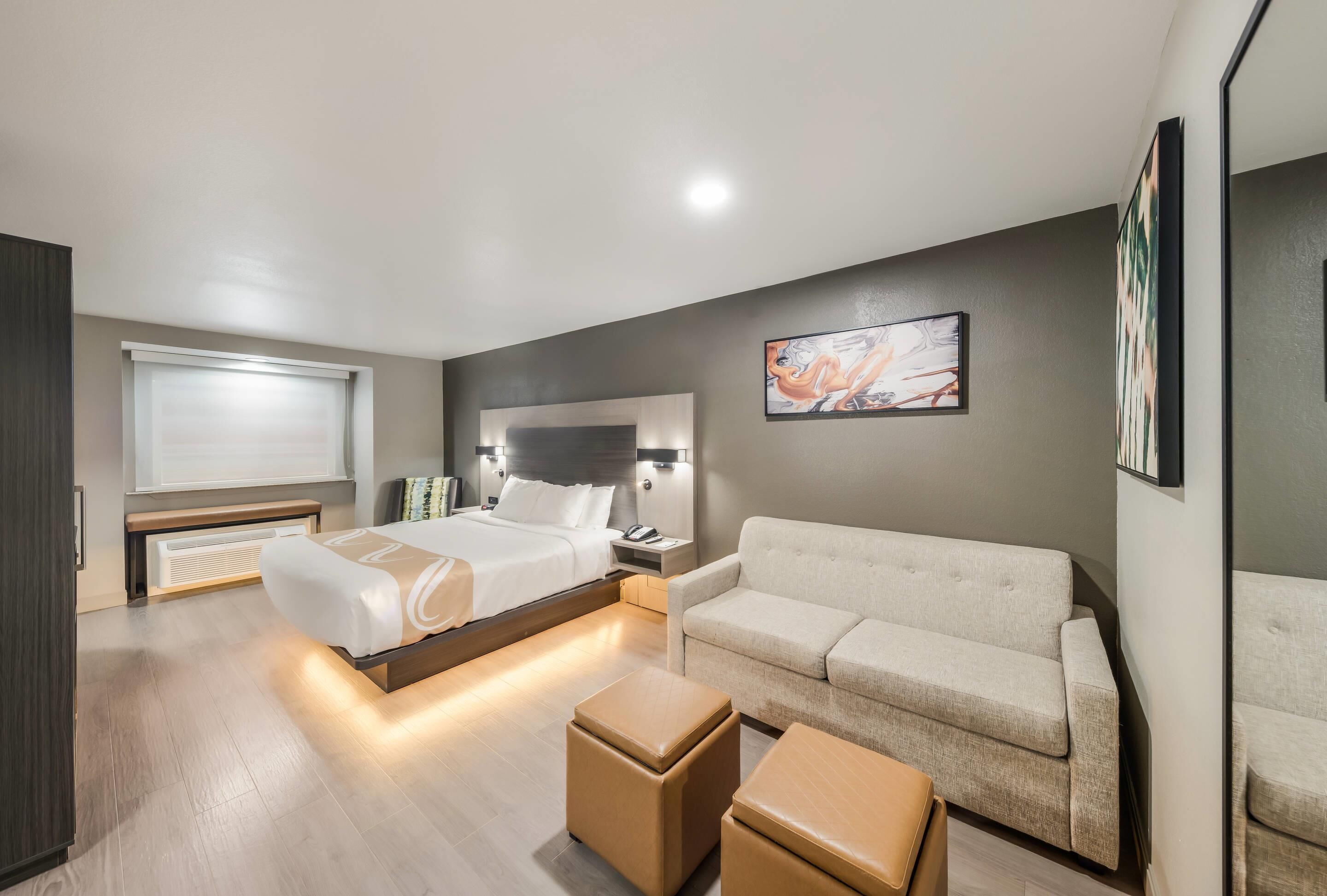 Habitación de hotel moderna con cama, sofá, una mesa de centro y un cuadro en la pared.