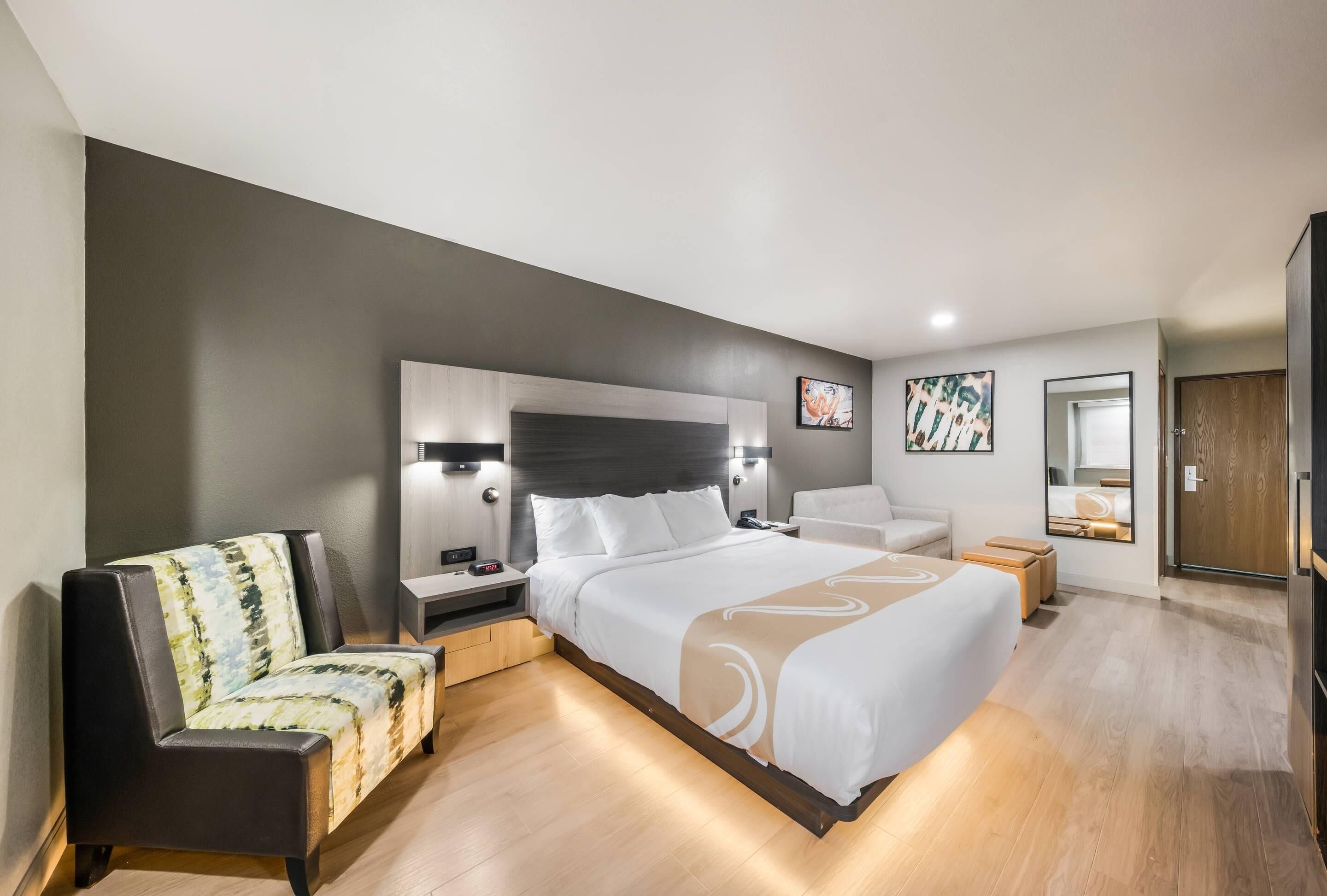 A modern hotel room with a large bed, a sofa, a nightstand, and a desk.