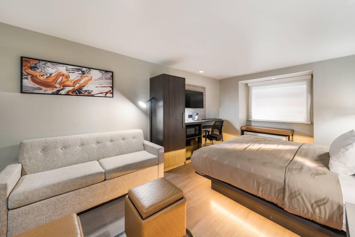 Une chambre d’hôtel moderne, équipée d’un canapé, d’un lit, d’un bureau et ornée d’un tableau au mur.