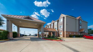 A multi-story hotel with a covered entrance, a parking lot, and a clear blue sky. - Quality Inn & Suites North Mesquite I-30 (Mesquite)