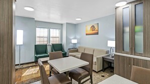 A hotel room with a dining area, two green chairs, a beige sofa, a table, and a cabinet. - Quality Inn & Suites North Mesquite I-30 (Mesquite)