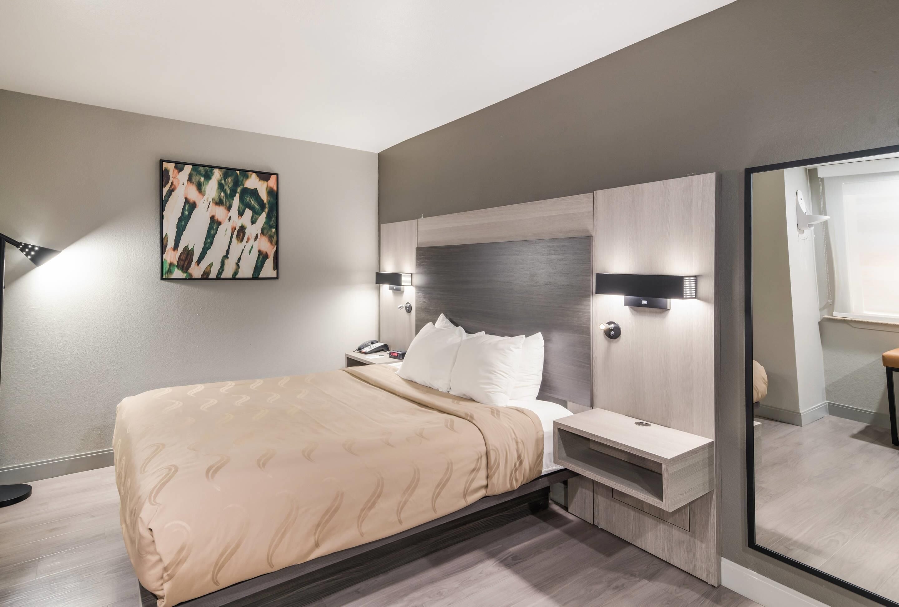 A modern bedroom with a large bed, bedside tables, a headboard with integrated lighting, a nightstand, and a wall-mounted artwork.