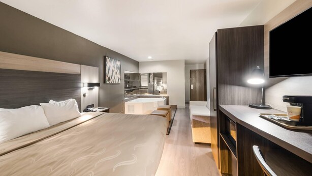 A modern hotel room with a large bed, a desk with a computer, a flat-screen TV, and a bathroom with a bathtub and shower. - Quality Inn & Suites North Mesquite I-30 (Mesquite)