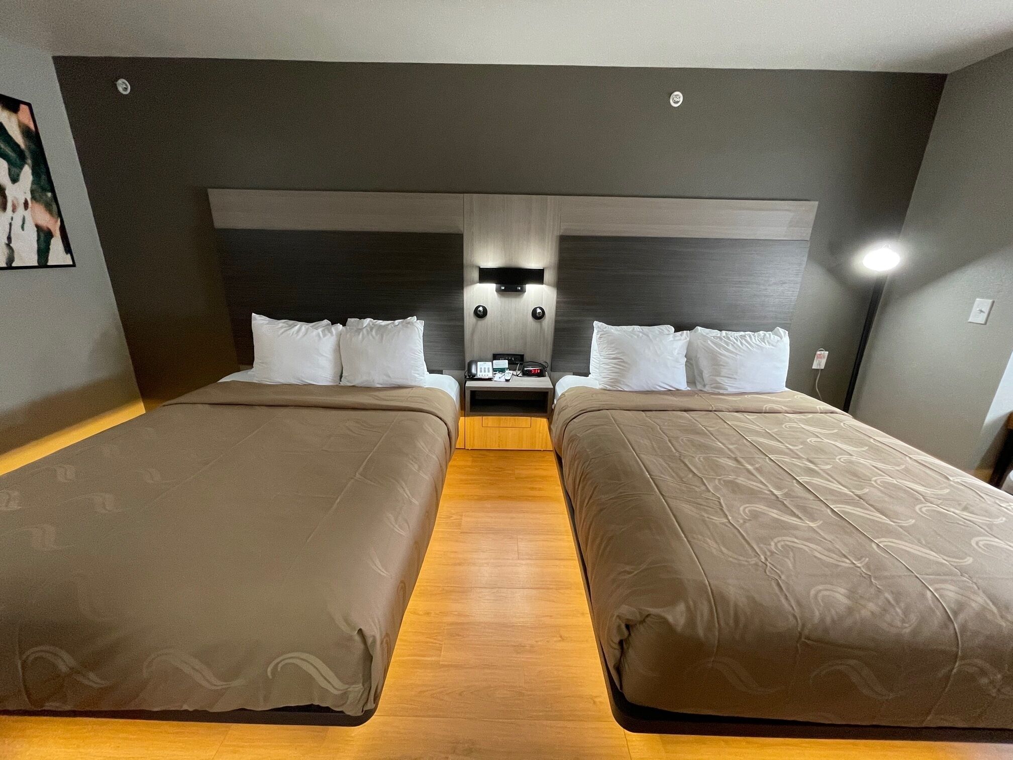 A hotel room with two beds, a nightstand, a wall-mounted phone, and a light fixture.