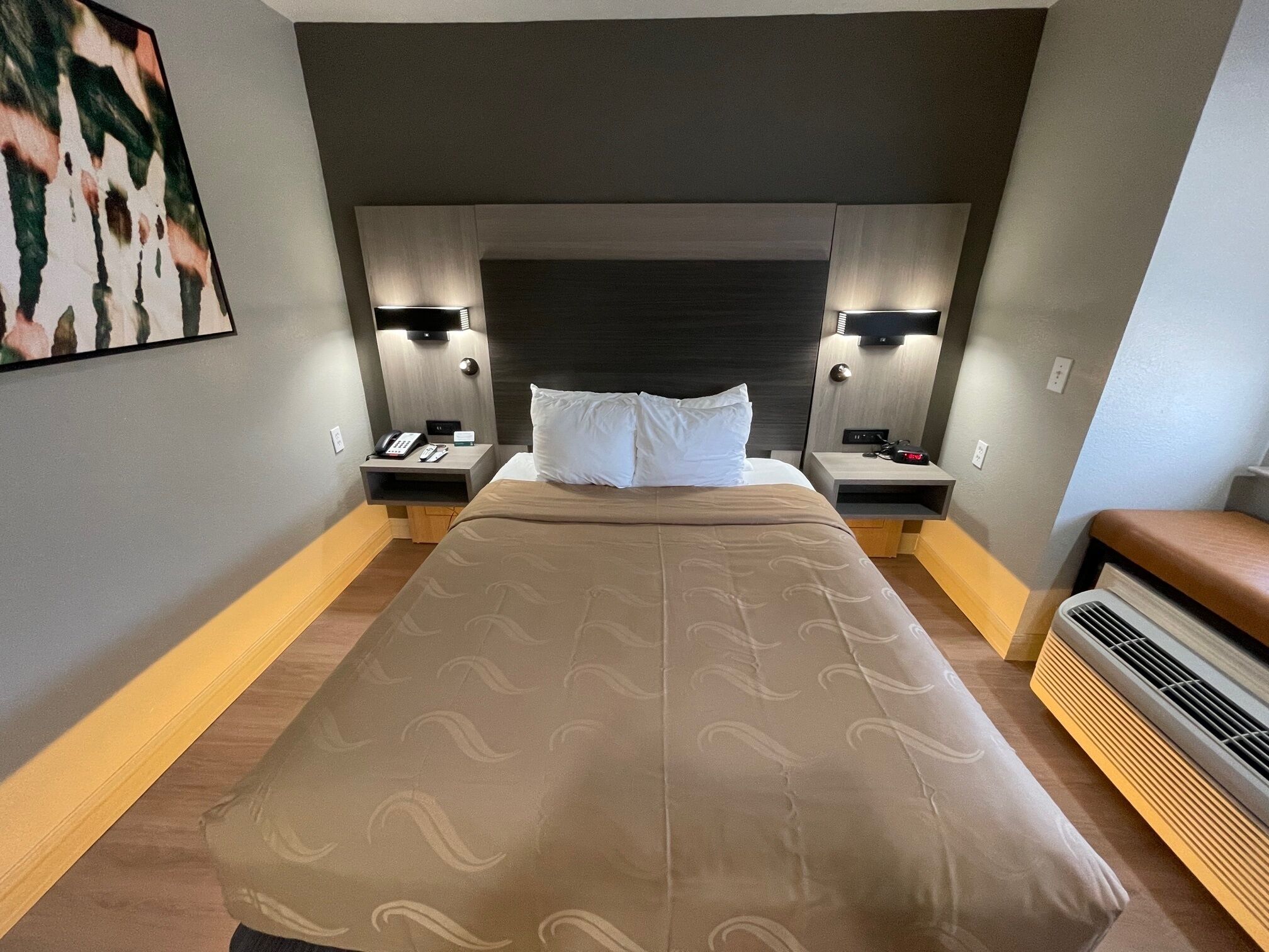 Habitación de hotel con una cama grande, mesitas de noche con lámparas, un televisor montado en la pared y un aire acondicionado también en la pared.